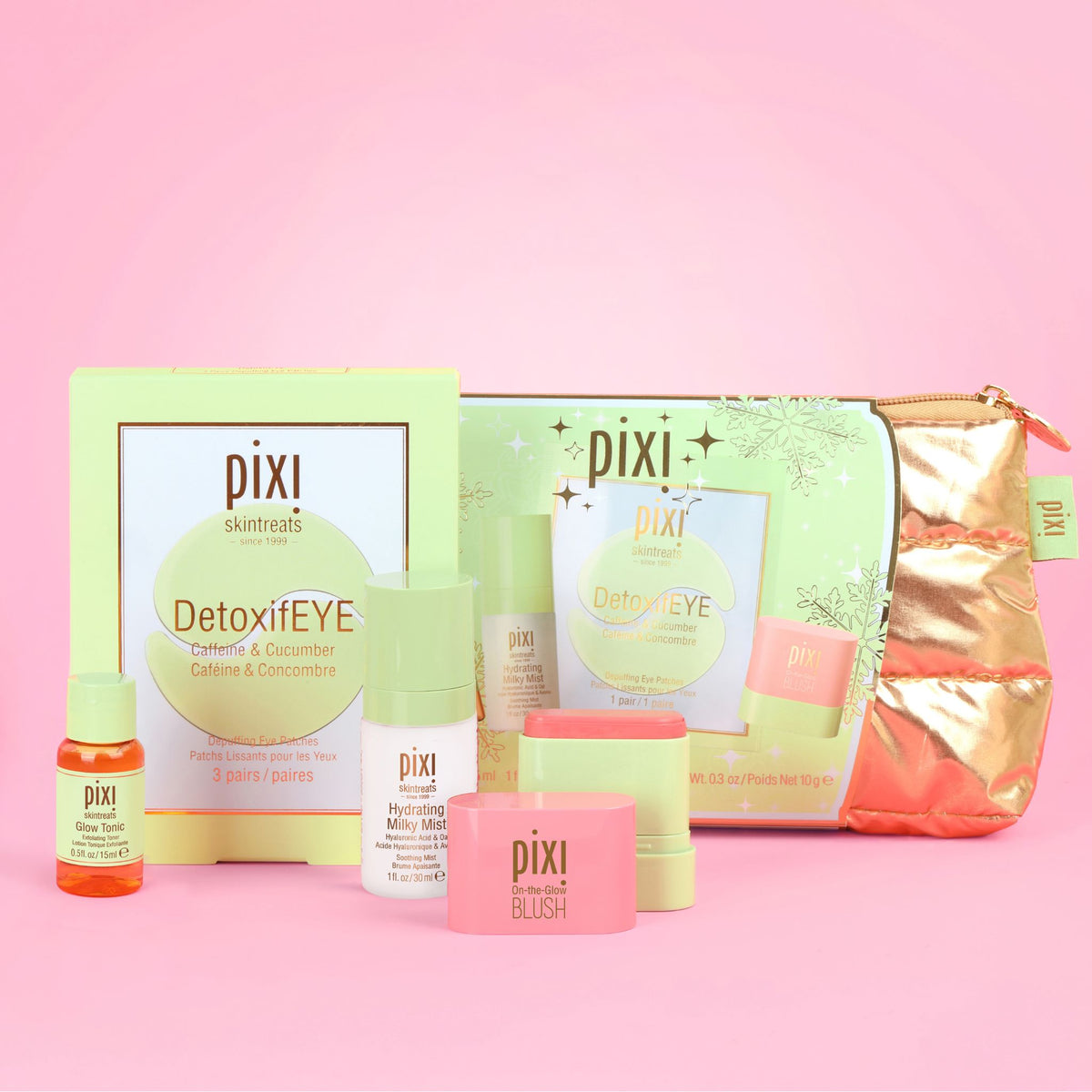 Pixi Skincare Heroes gift set arranged on a solid pink background, featuring a light green box, a metallic rose gold zip pouch, a small orange bottle, white and pink bottles, and a pink blush jar.
