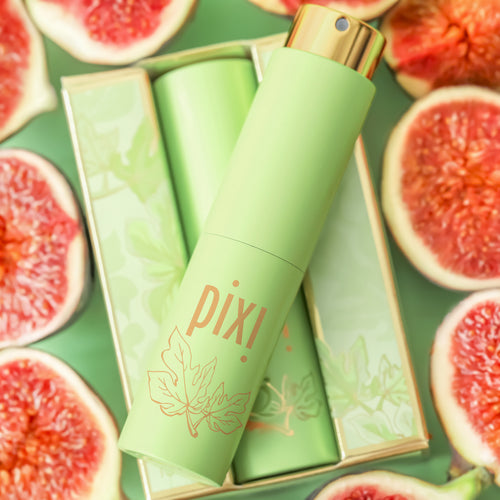A Pixi Perfume spray bottle in light green with a gold cap, displayed diagonally on top of its matching green box, surrounded by sliced pink figs on a green background. view 2