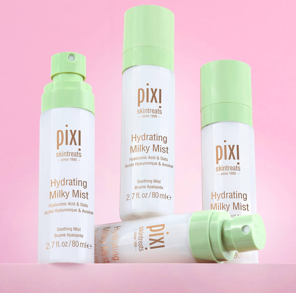 Three Pixi Skintreats Hydrating Milky Mist bottles in white and light green packaging, arranged on a solid pink background with one bottle lying down in front. view 1